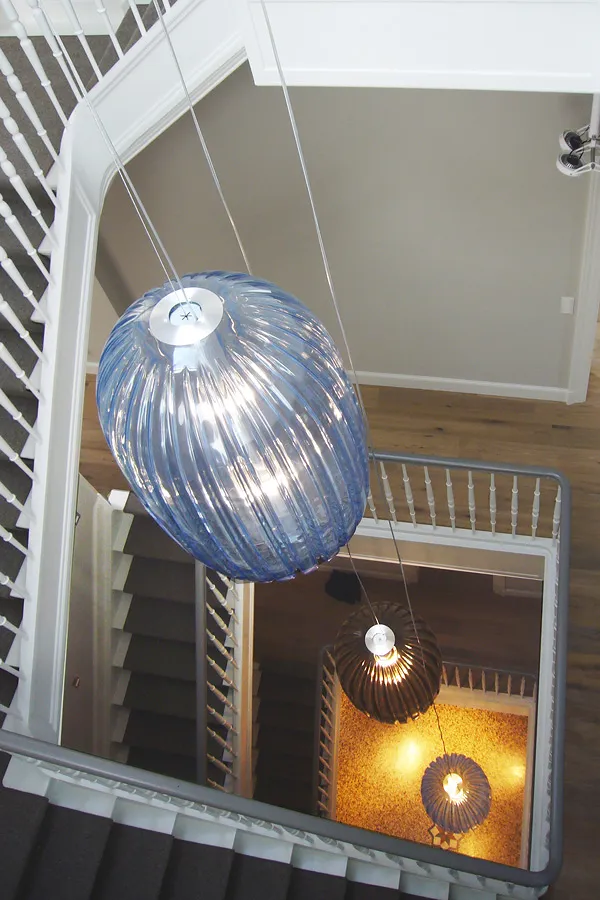 Blick von oben in ein Treppenhaus mit drei abgependelten großen Leuchten auf unterschiedlichen Höhen.