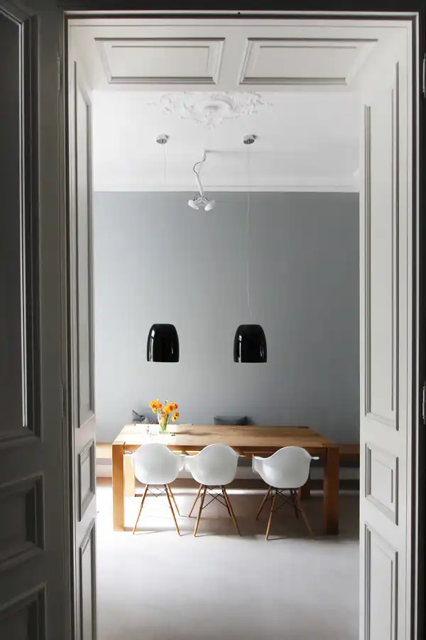 Über einem Esstisch aus Holz mit weißen Stühlen hängen zwei schwarze Leuchter 'Notte' von Prandina.